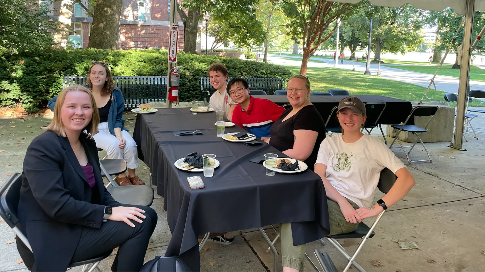 Group of 6 students sitting outside under a tent 